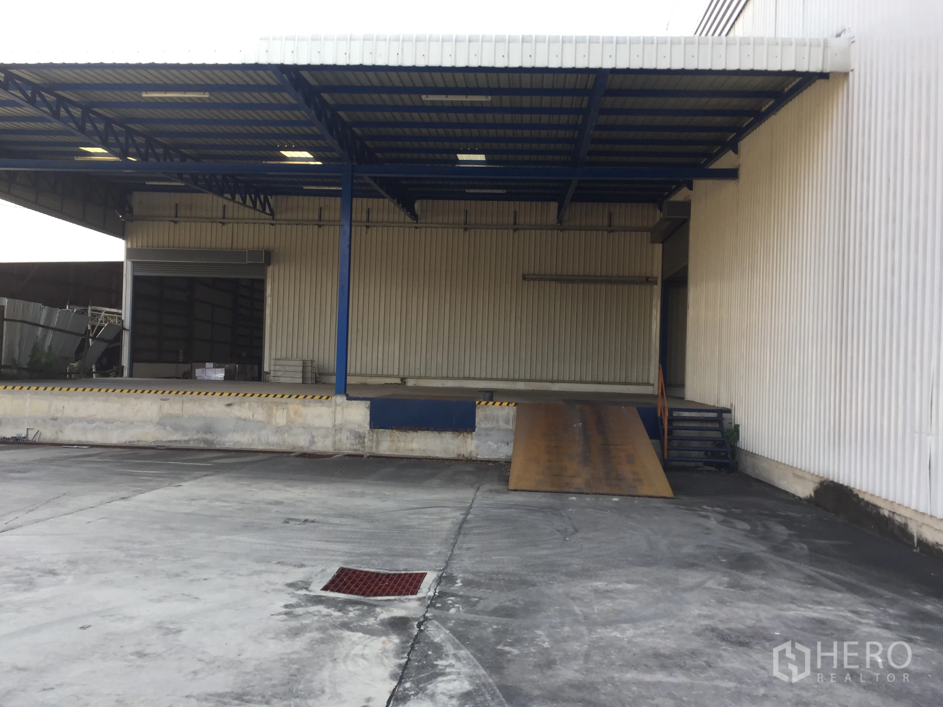 Warehouse for rent in Pak Kret, Nonthaburi - Dock-high loading area with canopy and ramp for truck access beside corrugated metal wall.