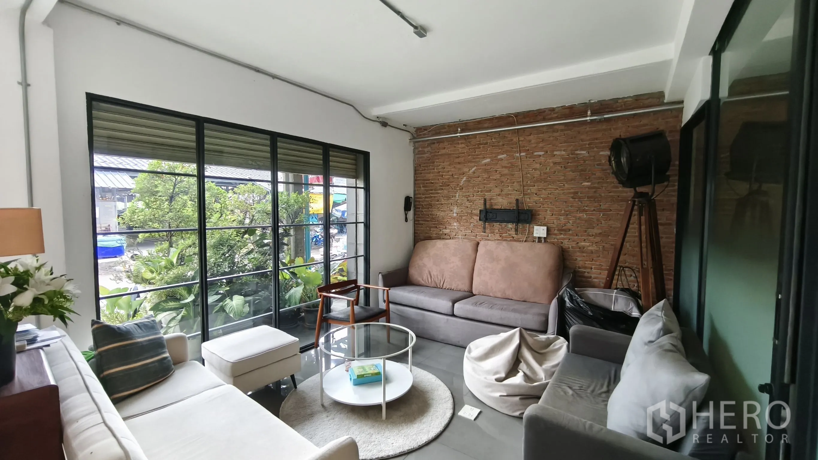 店屋 for rent in Khlong Toei, Bangkok - 起居休闲区，配多组沙发、黑框大窗景观绿植与砖面特色墙。