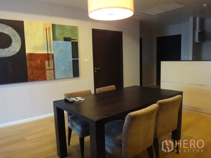 公寓 出租在Sathon, Bangkok - 餐区配深色木餐桌、四把软包椅、吊灯与抽象墙面装饰，临近厨房。