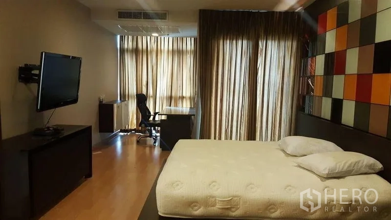Condominium for rent in Khlong Luang, Pathum Thani - Spacious bedroom with king bed, work desk by the window and floor-to-ceiling curtains.
