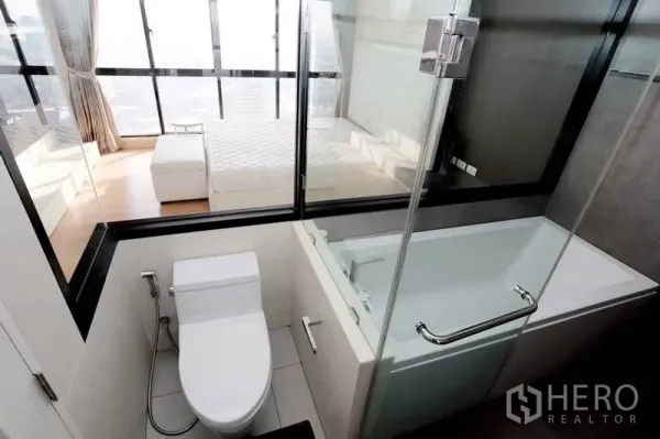 คอนโด ให้เช่าในKhlong San, Bangkok - ห้องน้ำโมเดิร์นพร้อมอ่างอาบน้ำและผนังกระจกมองไปยังห้องนอนวิวเมือง