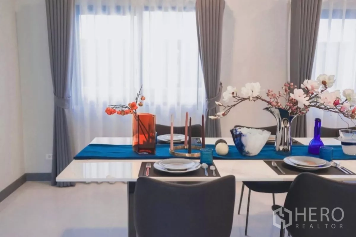 独立式住宅 出租在Bang Phli, Samut Prakan - 餐桌临双窗，灰色窗帘与花艺摆设点缀。