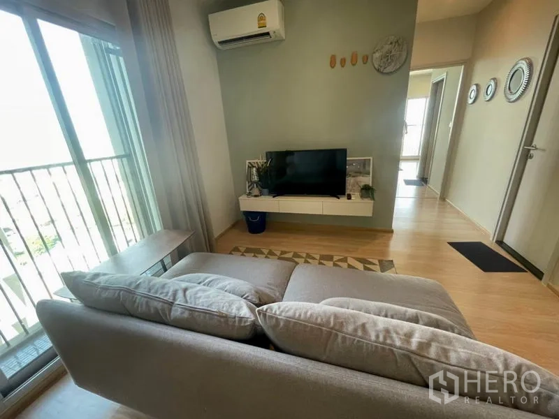Condominium for rent in Huai Khwang, Bangkok - Cozy living area with sofa facing TV wall and access to balcony.
