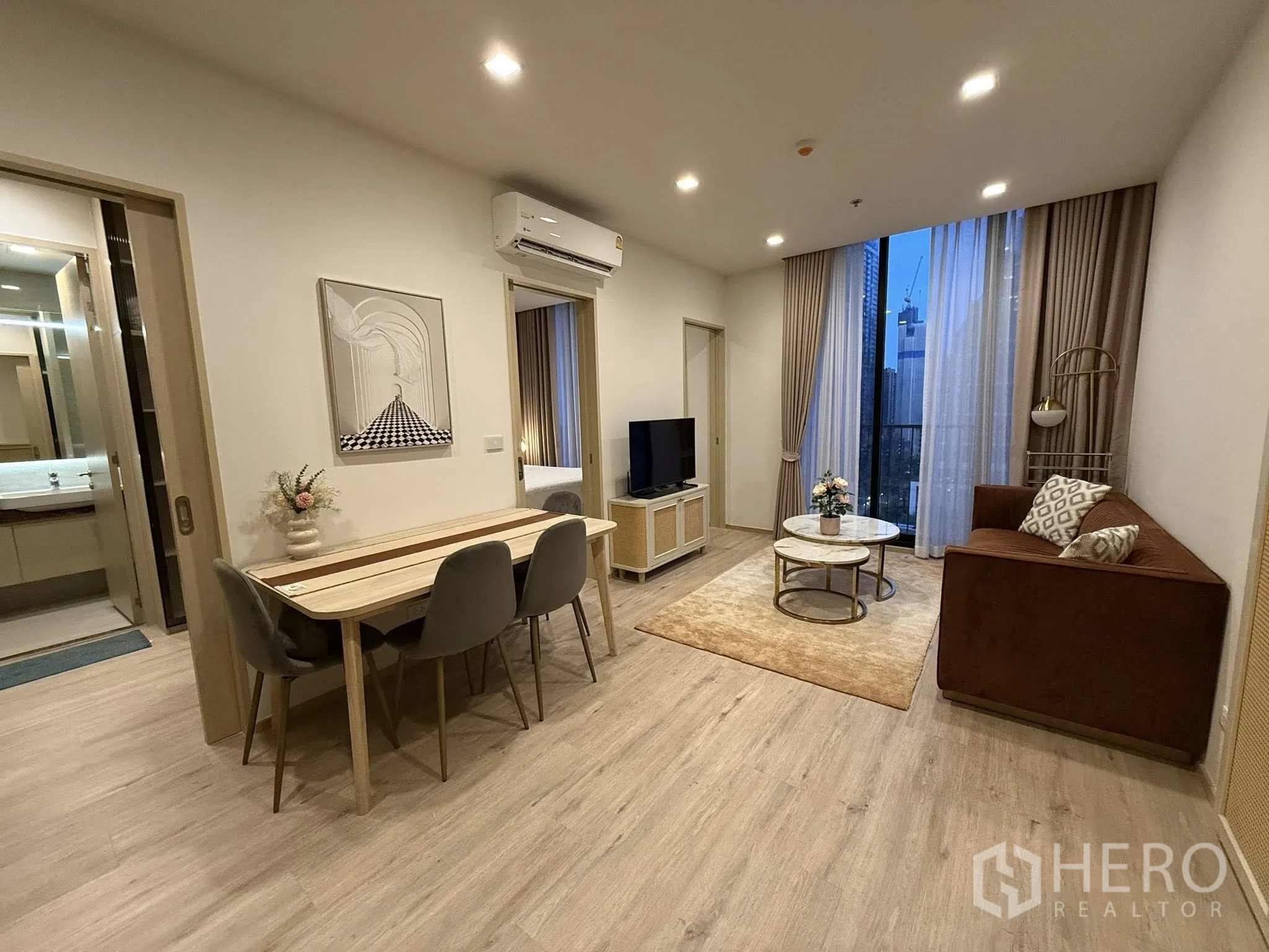 公寓 for rent in Watthana, Bangkok - 开放式客餐厅配沙发、电视、圆形茶几、四人餐桌与高窗城市景观。