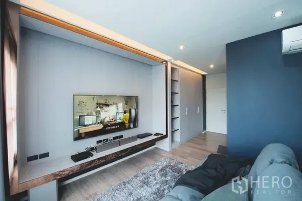 Townhouse for sale in Lak Si, Bangkok - Contemporary family room with wall-mounted TV, built-in shelves, and wood flooring.