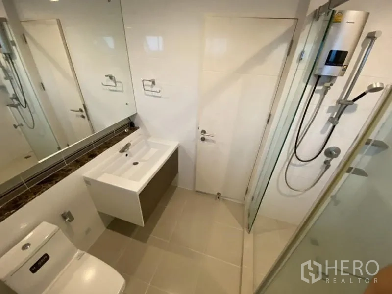 Detached House for rent in Bang Kapi, Bangkok - Contemporary bathroom with glass shower enclosure, large mirror and white fixtures.