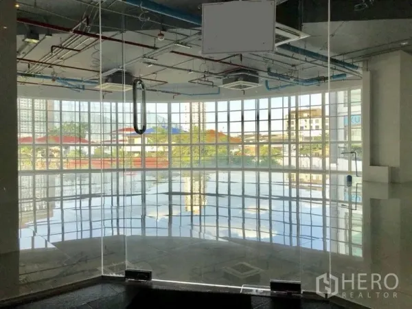 零售空间 出租在Khlong Toei, Bangkok - 曲面整面玻璃的零售单元，亮面瓷砖地与外露天花，透出城市景观。