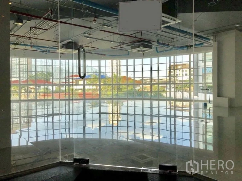 零售空间 出租在Khlong Toei, Bangkok - 曲面整面玻璃的零售单元，亮面瓷砖地与外露天花，透出城市景观。