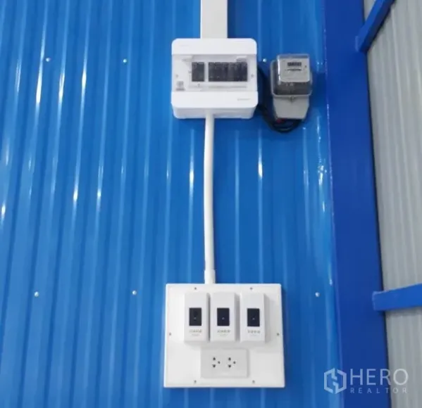 Warehouse for rent in Nong Chok, Bangkok - Close-up of electrical breaker panel and switches mounted on a blue corrugated wall inside the warehouse.