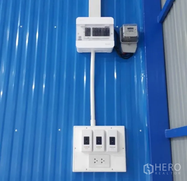 Warehouse for rent in Nong Chok, Bangkok - Close-up of electrical breaker panel and switches mounted on a blue corrugated wall inside the warehouse.
