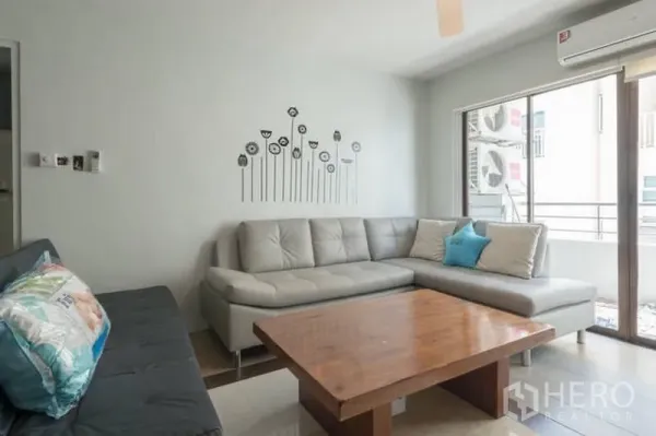 Condominium for rent in Watthana, Bangkok - Corner living space with L-shaped sofa, wooden coffee table, air conditioner, and balcony access.