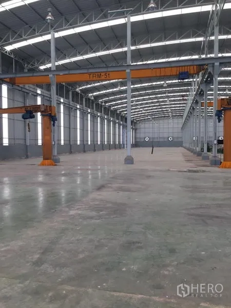 Factory for rent or sale in Samut Sakhon - High-roof warehouse interior with steel trusses and 5-ton overhead cranes along multiple bays.