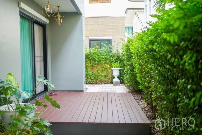 บ้าน ให้เช่าในSai Mai, Bangkok - ชานไม้มีหลังคาข้างประตูกระจกบานเลื่อน ล้อมด้วยแนวพุ่มไม้