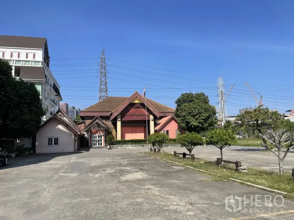 พื้นที่ขายปลีก ให้เช่าในSuan Luang, Bangkok - มุมกว้างของโครงการพื้นที่ค้าปลีก พร้อมลานคอนกรีตจอดรถ ต้นไม้ และอาคารทรงจั่วในสวนหลวง