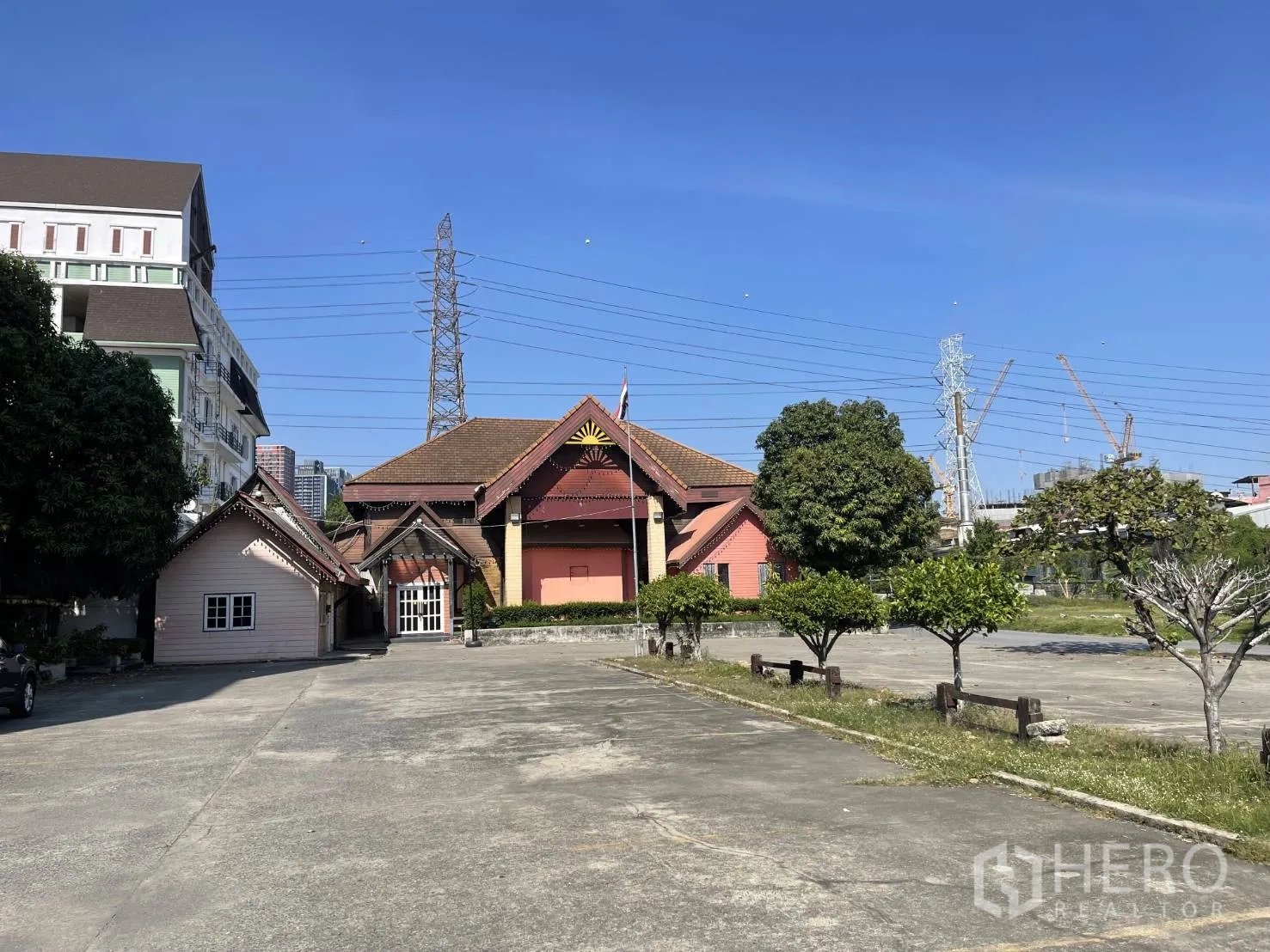 พื้นที่ขายปลีก ให้เช่าในSuan Luang, Bangkok - มุมกว้างของโครงการพื้นที่ค้าปลีก พร้อมลานคอนกรีตจอดรถ ต้นไม้ และอาคารทรงจั่วในสวนหลวง