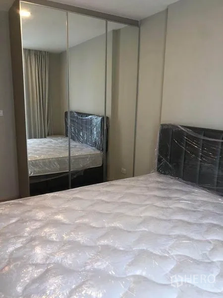 คอนโด for ในWatthana, Bangkok - ห้องนอนสว่างในคอนโดย่านวัฒนา ตู้เสื้อผ้าบานกระจก เฮดบอร์ดและผ้าม่านโทนอ่อน