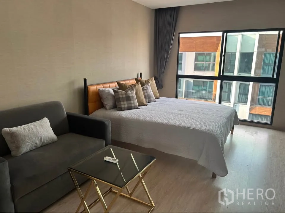 Townhouse for rent in Suan Luang, Bangkok - Bright bedroom with king bed, sofa and large windows overlooking the townhouse community.