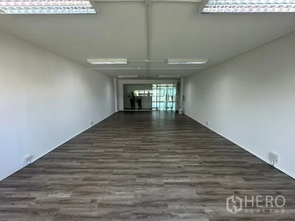 办公空间 出租在Bangkok - 开放式办公室，木纹地板、白色墙面、荧光灯天花，尽头带玻璃入口。