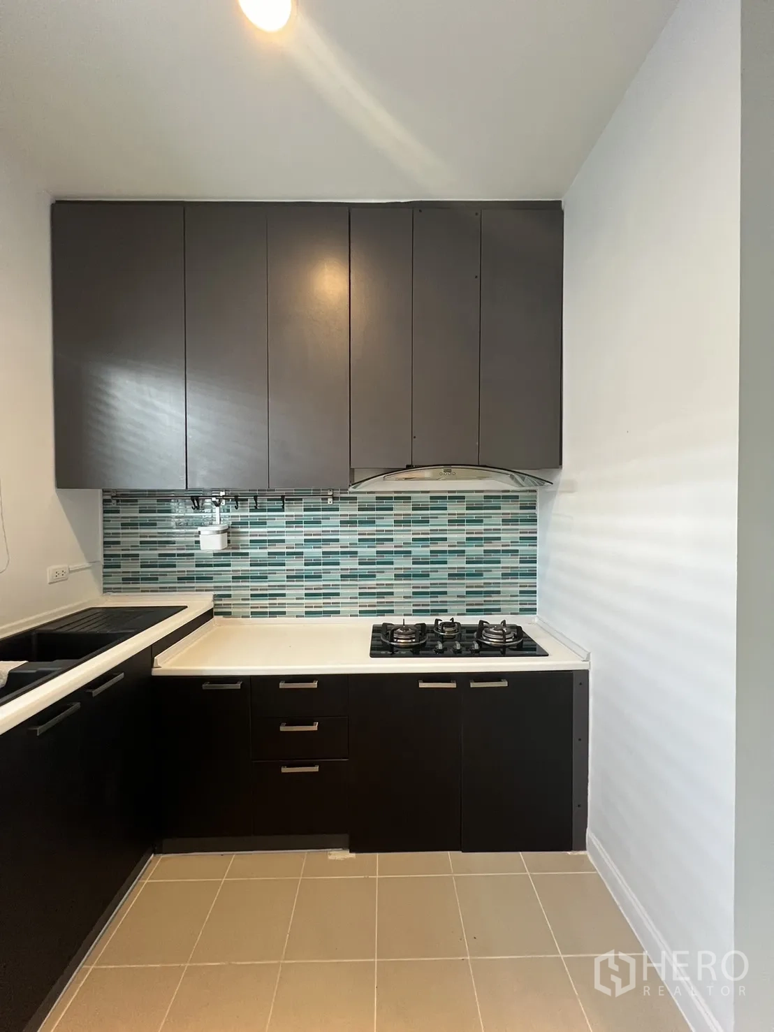 Townhouse for rent in Wang Thonglang, Bangkok - L-shaped kitchen with dark cabinets, white countertop and gas hob.