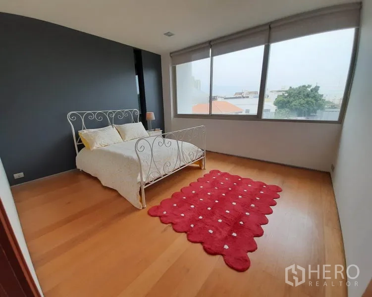 คอนโด ให้เช่าในKhlong Toei, Bangkok - ห้องนอนรองสว่างไสว มีหน้าต่างบานใหญ่ เตียงโครงเหล็ก และพรมสีแดงบนพื้นไม้.