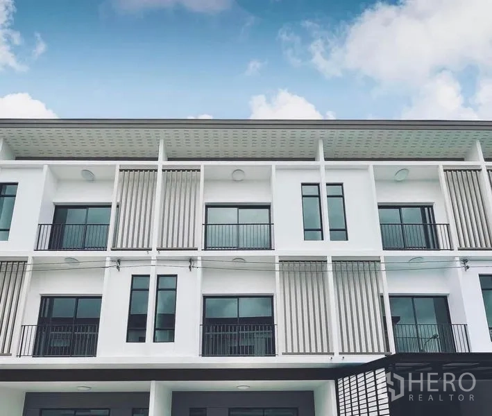 Townhouse for rent in Bang Kapi, Bangkok - Modern three-storey townhouse facade with balconies and vertical screens against a blue sky in Bang Kapi, Bangkok.