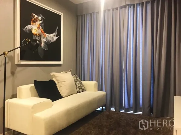 Condominium for sale in Khlong Toei, Bangkok - Cozy lounge with a white sofa, floor lamp and full-height curtains.
