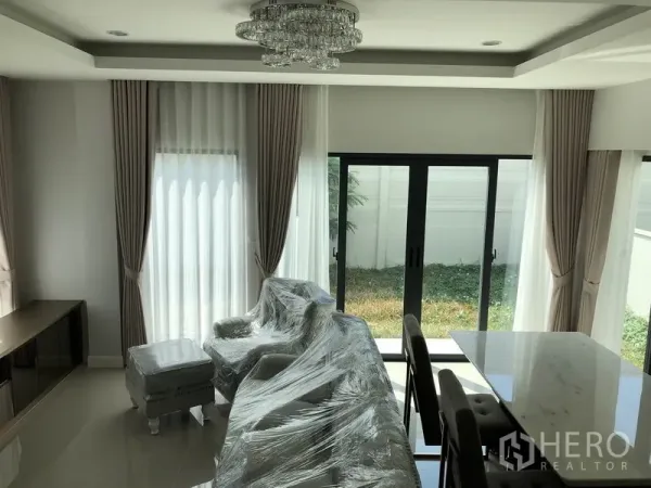 独立式住宅 出租在Prawet, Bangkok - 采光充足的客厅，落地窗帘与水晶吊灯，推拉门通向草坪。