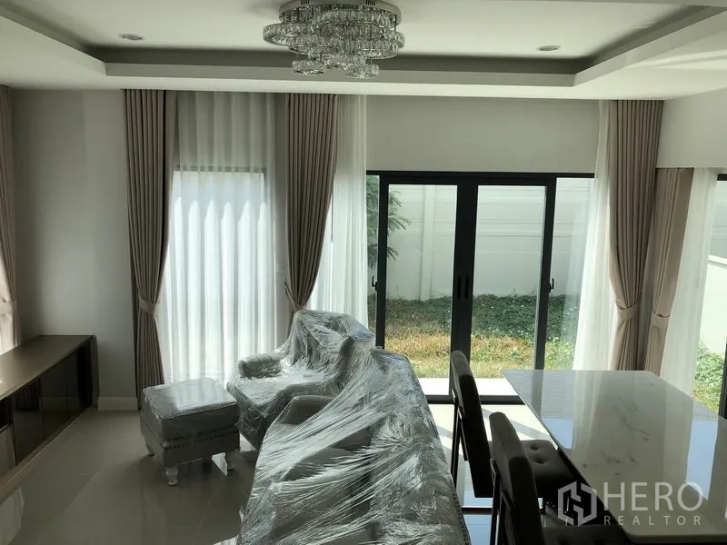 独立式住宅 出租在Prawet, Bangkok - 采光充足的客厅，落地窗帘与水晶吊灯，推拉门通向草坪。