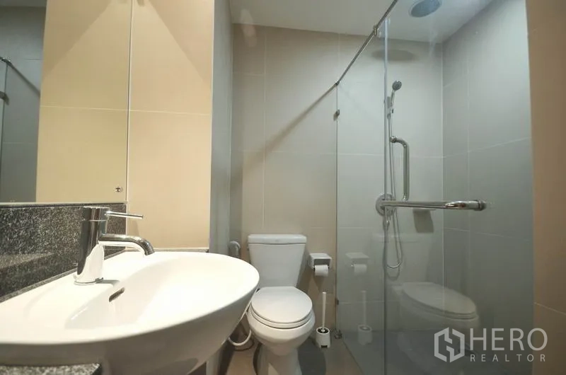 公寓 出租或出售在Watthana, Bangkok - 现代浴室，玻璃淋浴房、顶喷花洒、白色台盆与坐便器。