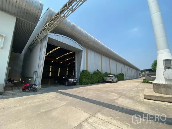 Factory for rent or sale in Samut Sakhon - Factory exterior in Ban Phaeo, Samut Sakhon with wide concrete yard, large loading entrance and metal ventilation ducts.