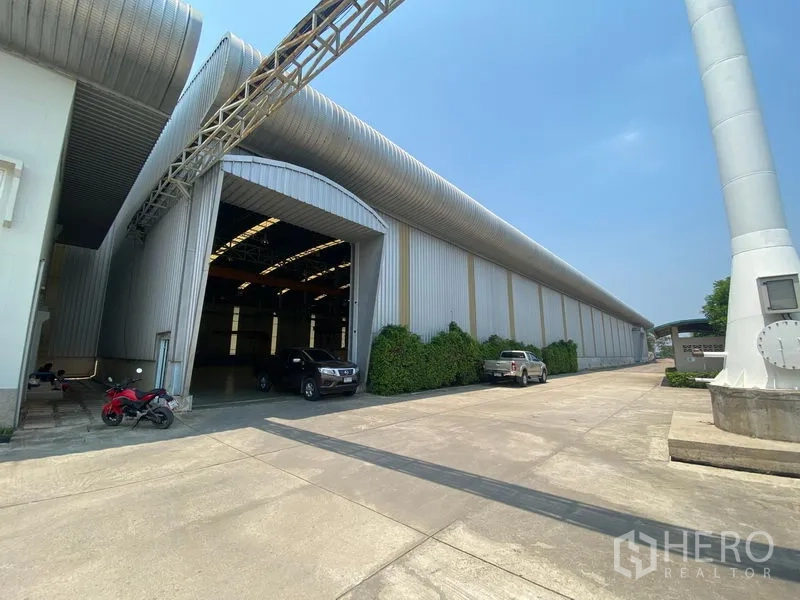Factory for rent or sale in Samut Sakhon - Factory exterior in Ban Phaeo, Samut Sakhon with wide concrete yard, large loading entrance and metal ventilation ducts.