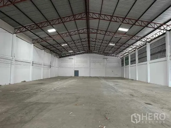 Warehouse for rent in Mueang Samut Sakhon, Samut Sakhon - Empty warehouse hall with red steel trusses, clear-span space and power conduits along white walls.