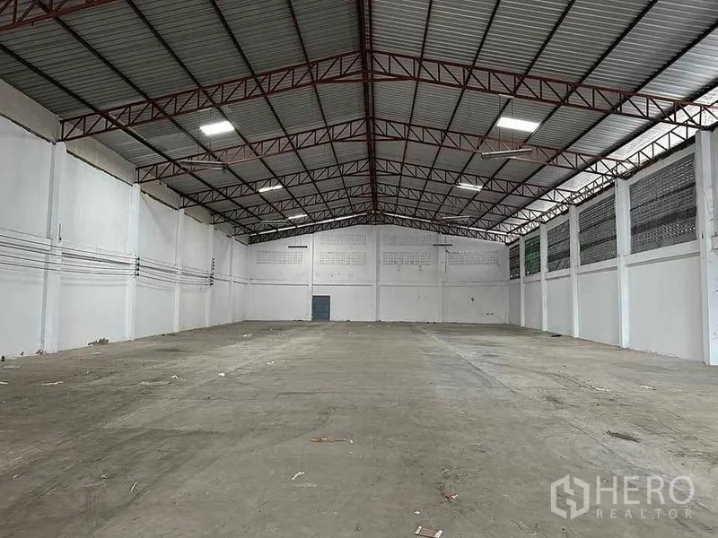 Warehouse for rent in Mueang Samut Sakhon, Samut Sakhon - Empty warehouse hall with red steel trusses, clear-span space and power conduits along white walls.