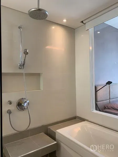 Condominium for rent in Watthana, Bangkok - Bathroom with rain shower, bathtub and niche shelving next to a window linked to the bedroom.