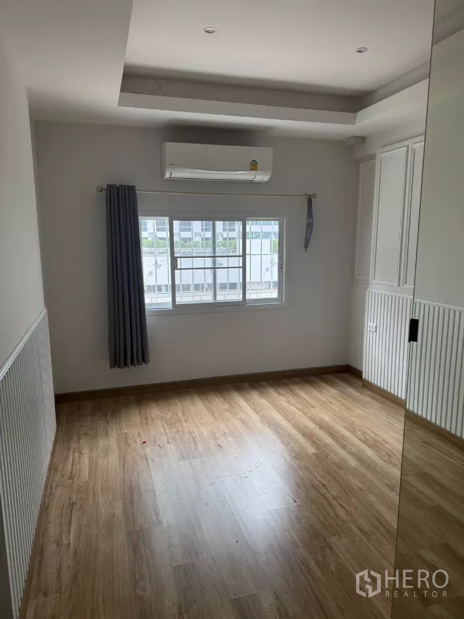 Shophouse for rent - Sunlit room with wood-look flooring, window AC, and white paneled walls.