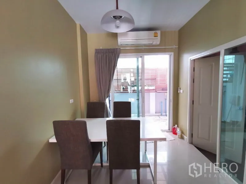 联排别墅 出租在Wang Thonglang, Bangkok - 餐厅配四把椅子、吊灯与空调，推拉玻璃门通往小阳台。