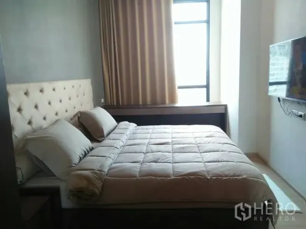 Condominium for rent in Huai Khwang, Bangkok - Bright master bedroom with large window, wall-mounted TV and padded headboard.