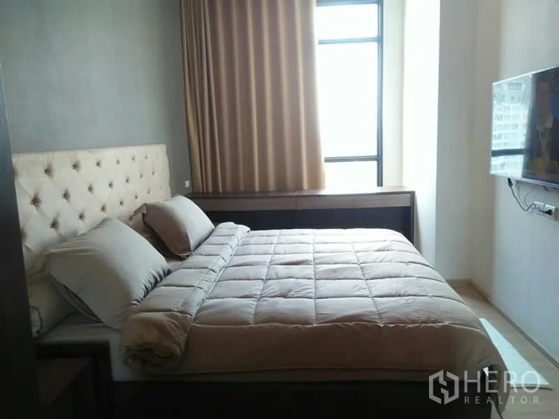 Condominium for rent in Huai Khwang, Bangkok - Bright master bedroom with large window, wall-mounted TV and padded headboard.
