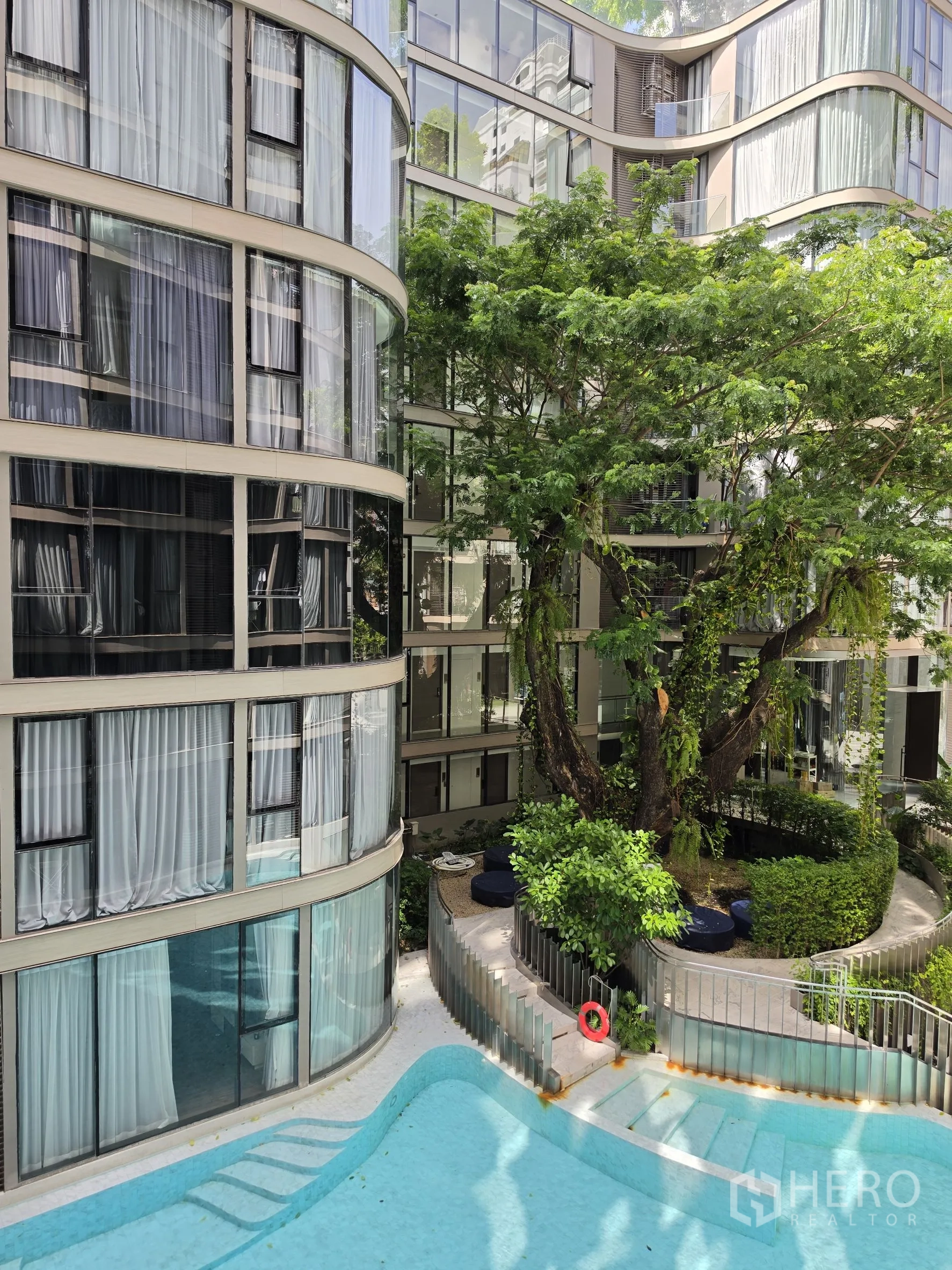 คอนโด for rent in Khlong Toei, Bangkok - คอร์ตยาร์ดสระว่ายน้ำล้อมรอบด้วยต้นไม้และอาคารกระจกโค้ง