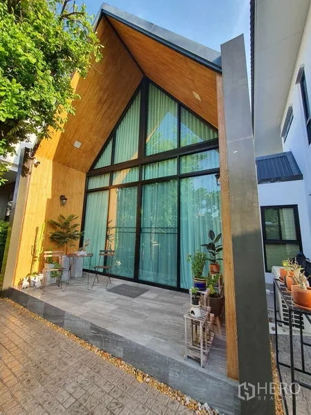Detached House for sale in Bang Khun Thian, Bangkok - Front elevation featuring dramatic A-frame glazing and cozy plant-lined terrace.