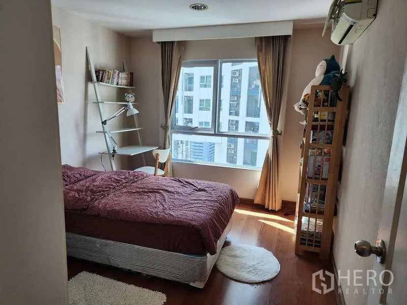 Condominium for rent in Huai Khwang, Bangkok - Second bedroom with bed, study desk and shelving beside a bright window.