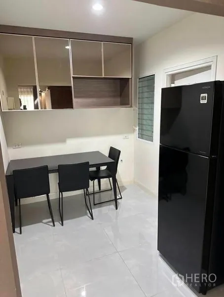 Detached House for rent in Suan Luang, Bangkok - Compact dining nook beside a tall black refrigerator and overhead storage cabinets.