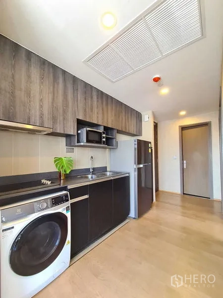 Condominium for rent in Bang Rak, Bangkok - Kitchen corridor with sink, cooktop, overhead storage and full-size fridge.