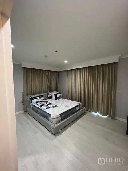 Condominium for sale in Sathon, Bangkok - Spacious master bedroom with king bed, light wood flooring, and full-height blackout curtains.