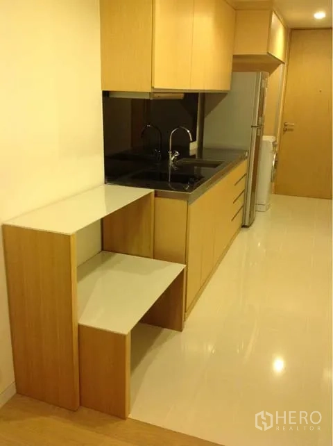 Condominium for rent or sale in Watthana, Bangkok - Compact kitchenette with light wood cabinets, black countertop and refrigerator