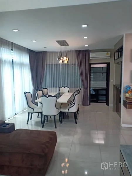 Detached House for rent in Thanyaburi, Pathum Thani - Dining space with six upholstered chairs, chandelier, and corner windows with curtains.