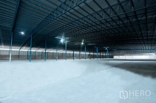 Warehouse for rent in Pathum Thani - Vast warehouse interior with high steel truss roof, concrete floor, and ample lighting.