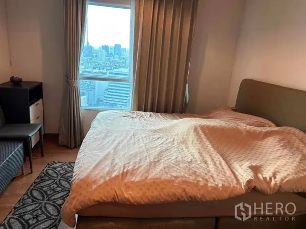 Condominium for sale in Huai Khwang, Bangkok - Bedroom with large bed, floor-to-ceiling curtains and a window showing Bangkok city views.
