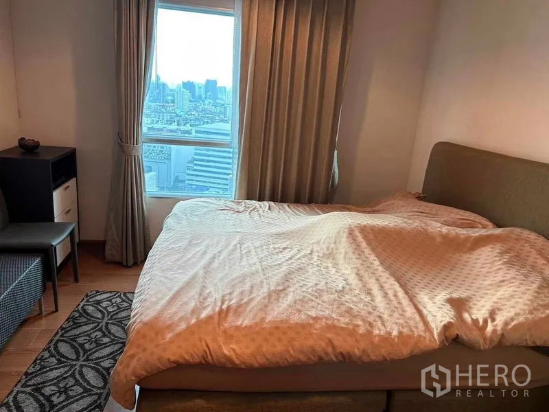 Condominium for sale in Huai Khwang, Bangkok - Bedroom with large bed, floor-to-ceiling curtains and a window showing Bangkok city views.