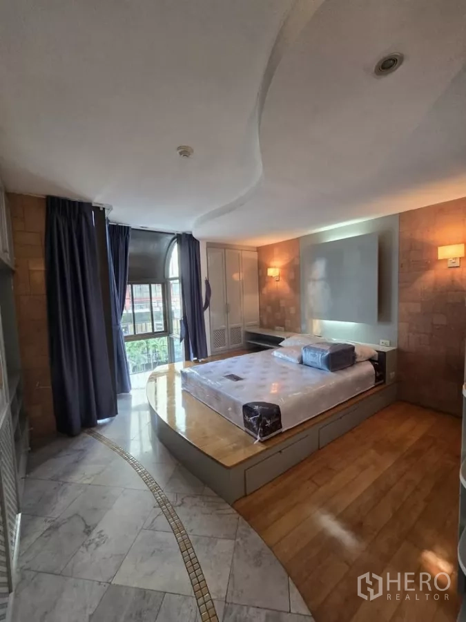 Condominium for rent in Pathum Wan, Bangkok - Bedroom with platform bed, bay window and mixed marble and wood flooring.